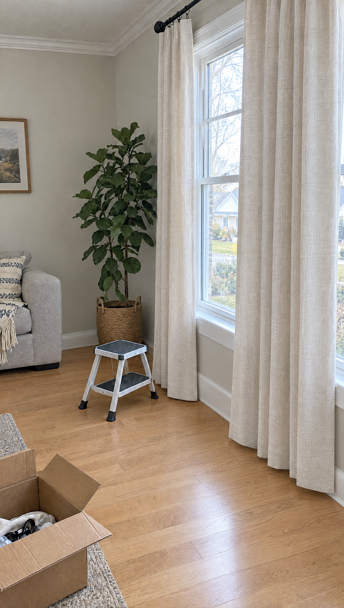 A living room window with two curtain panels hanging level just above the floor