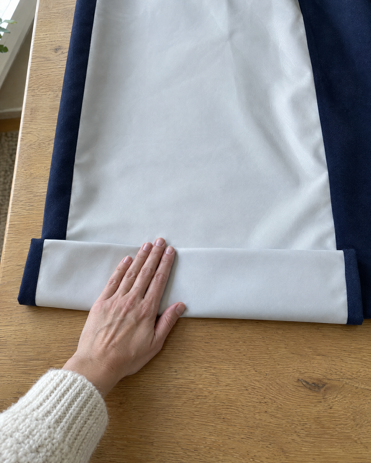 A hand pressing a hem on the coated back of a blackout curtain