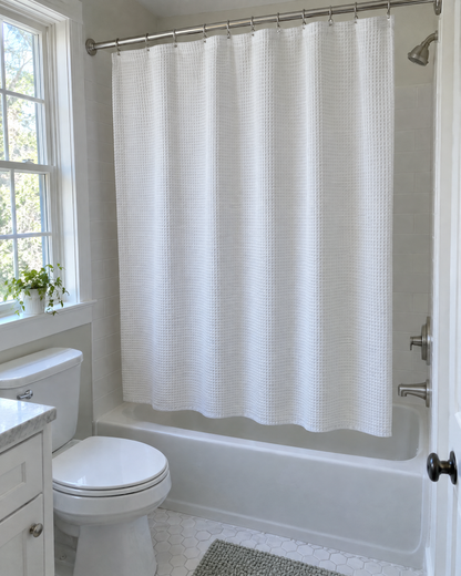 A fabric shower curtain with a neat hem hanging at a bathtub
